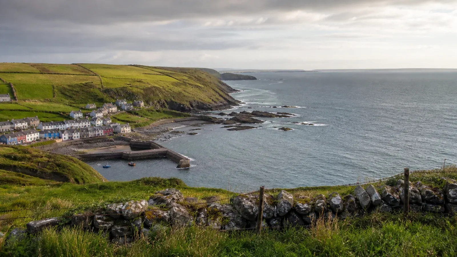 Vila portuária na costa atlântica de Cork, entre encostas verdes e uma baía rochosa